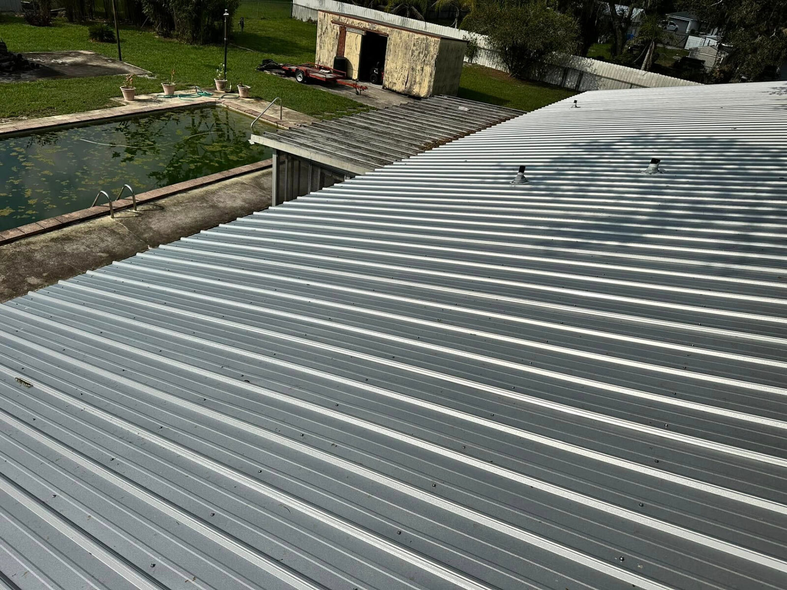 New metal roof panels with pipe boots beside a backyard pool